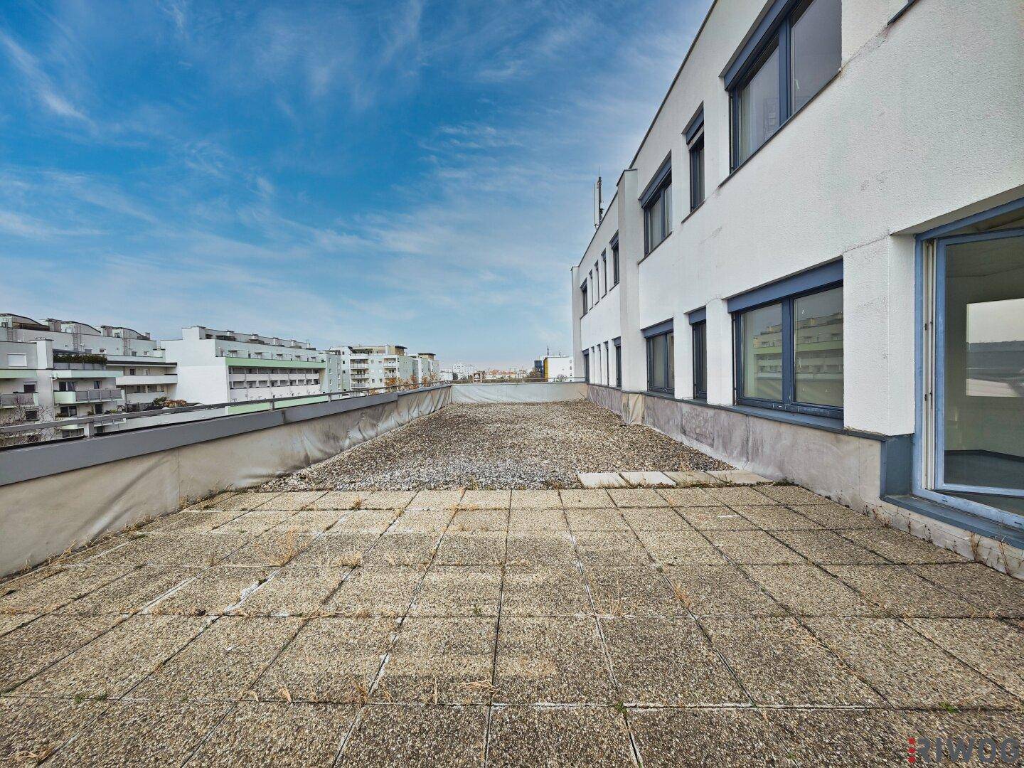 Große, geflieste Dachterrasse mit weitem Blick über die Stadt und angrenzendem Gebäude.