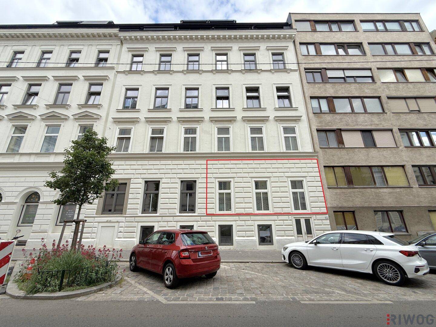 Ansicht der Gebäudefassade von der Straße mit geparkten Autos und klassischer Architektur.