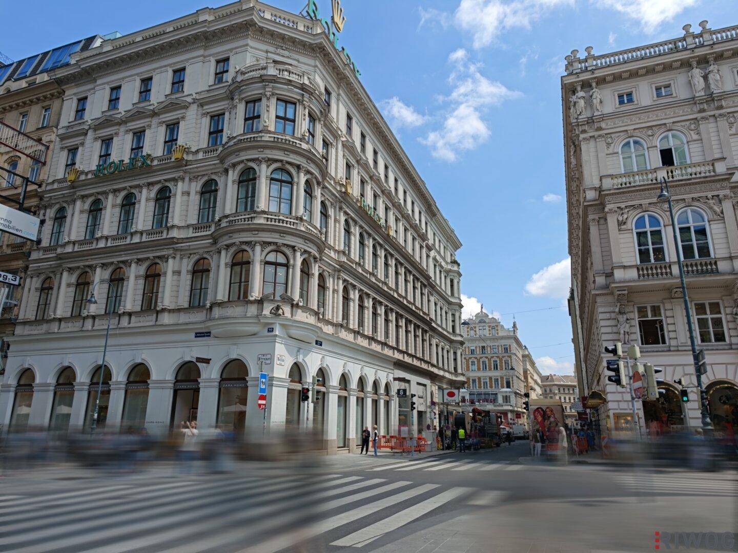 Elegantes Eckgebäude in der Wiener Innenstadt mit Geschäften im Erdgeschoss und belebter Kreuzung.