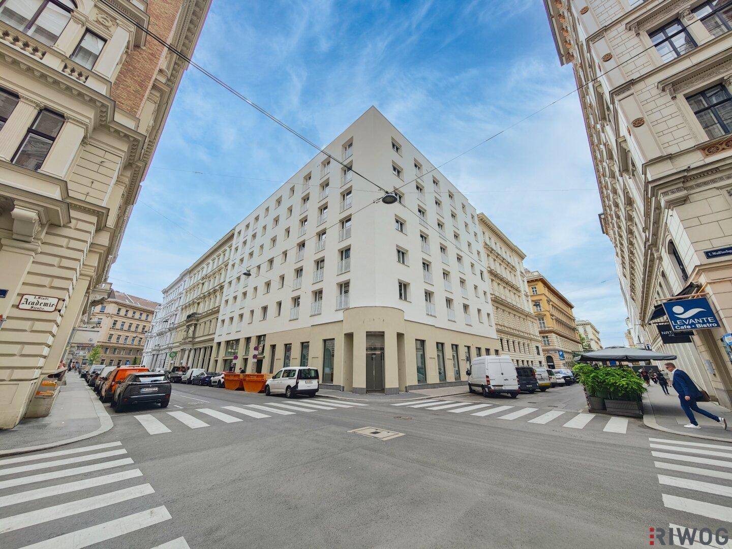 Modernes Eckgebäude in der Stadt mit klaren Linien und umliegenden historischen Gebäuden.