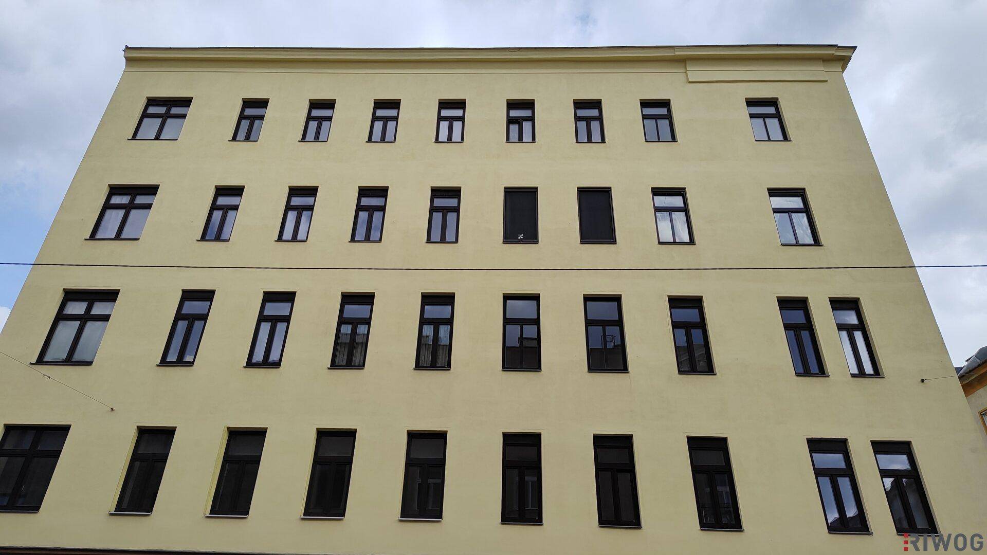 Frontansicht eines gelben Gebäudes mit zahlreichen Fenstern und dunklen Rahmen.