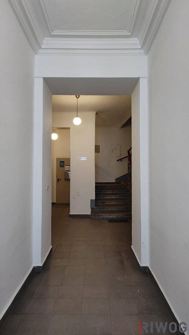 Langer Flur mit dunklen Fliesen und einem Blick auf das Treppenhaus im Hintergrund.