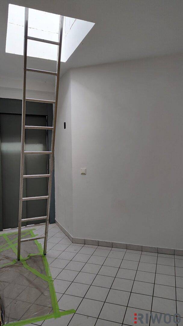 Raum mit weiß gefliestem Boden und einer Leiter, die zu einem Dachfenster führt.