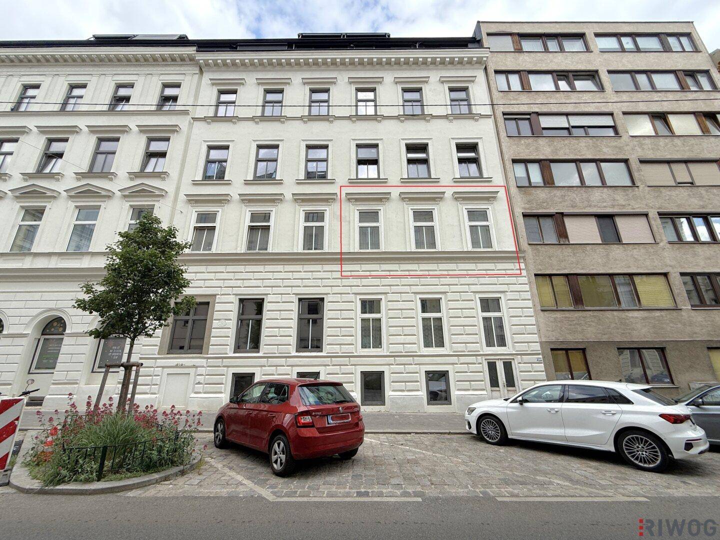 Ansicht der modernen Gebäudefassade mit mehreren Stockwerken und geparkten Autos auf der Straße.