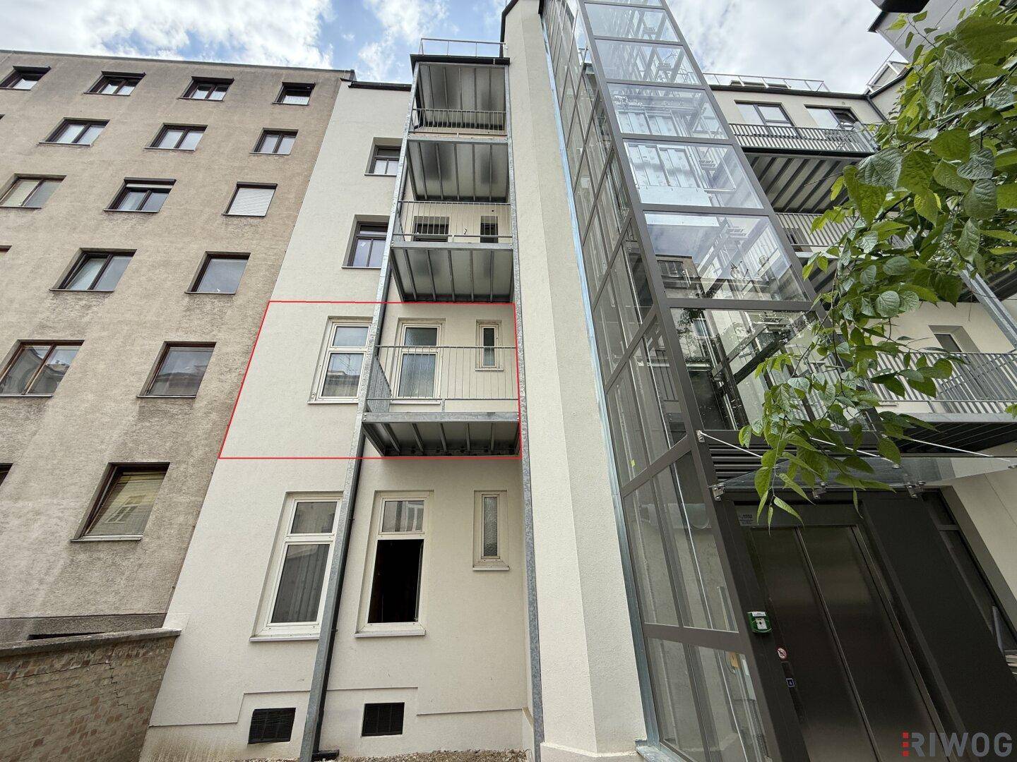 Seitenansicht des Gebäudes mit einem externen Glasaufzug und mehreren Balkonen.