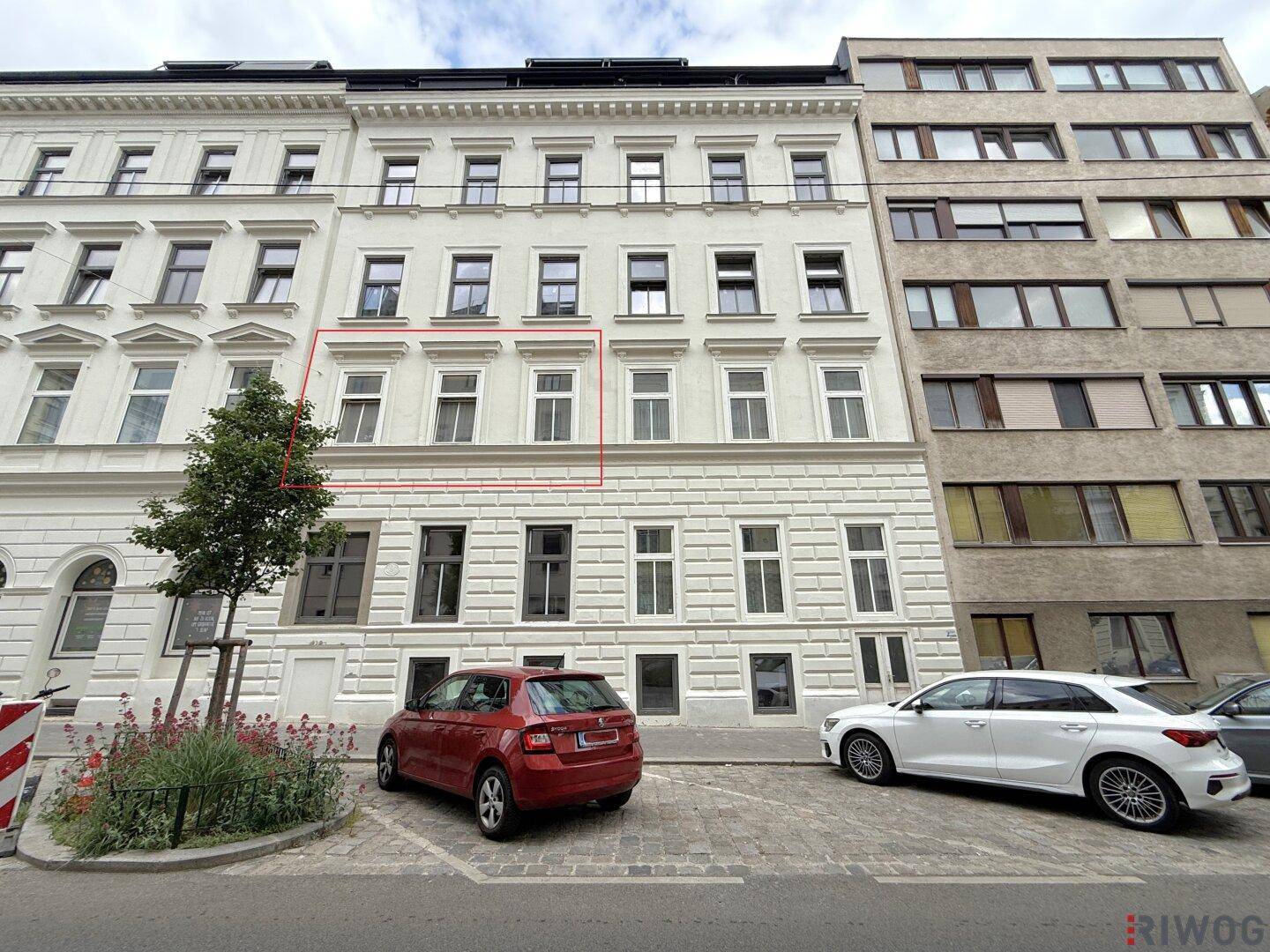 Ansicht der modernen Fassade eines Mehrfamilienhauses mit vielen Fenstern und geparkten Autos.
