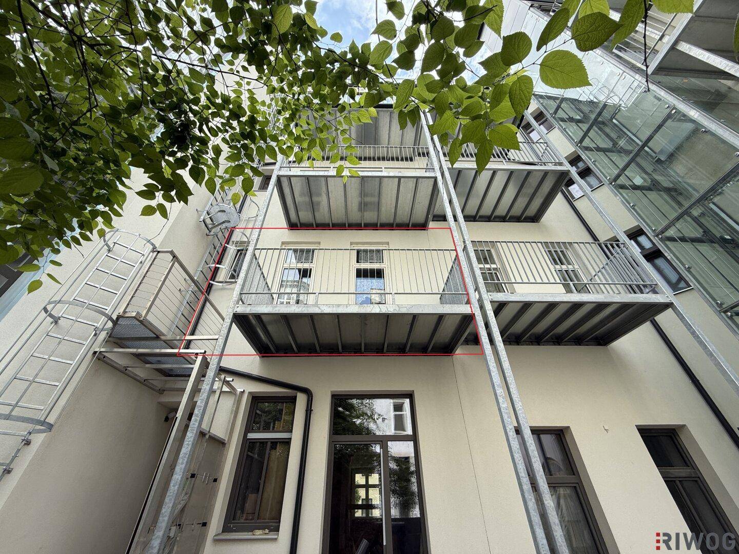 Blick auf die Rückseite des Gebäudes mit mehreren Metallbalkonen und einem externen Glasaufzug.