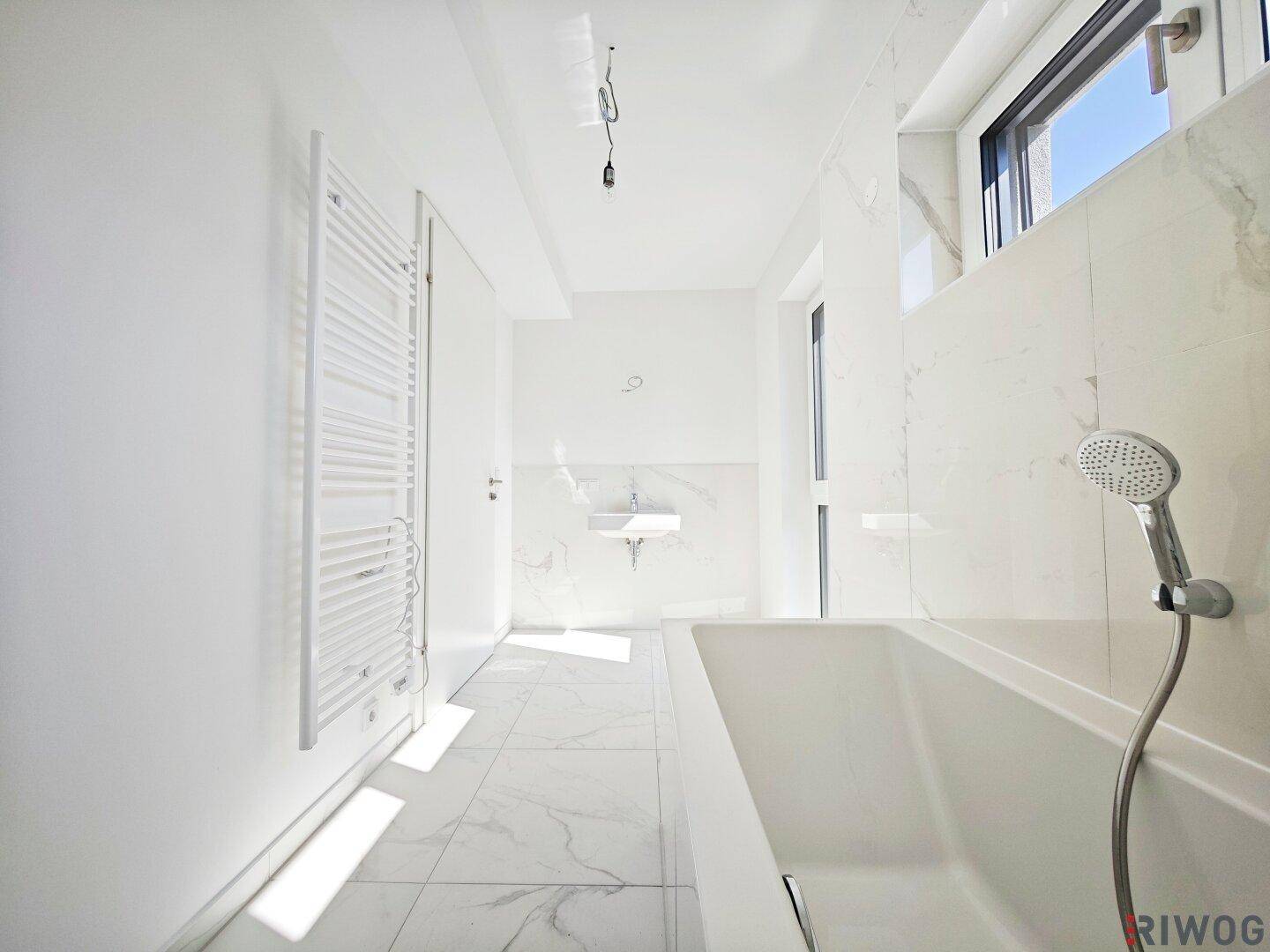 Elegantes Badezimmer mit Badewanne, beheiztem Handtuchhalter und modernen Marmorfliesen.