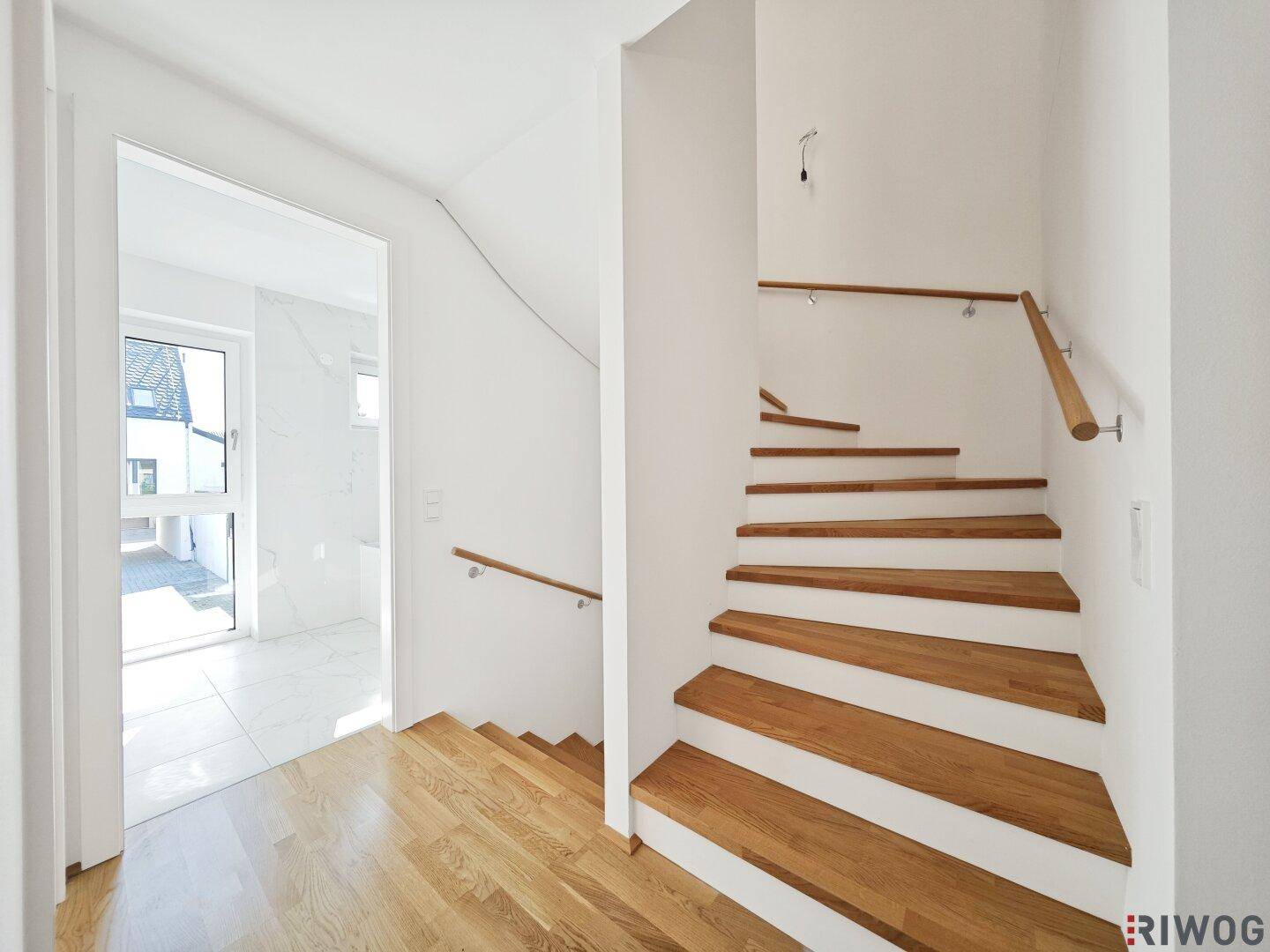 Heller Eingangsbereich mit Holztreppe und modernem Fliesenboden, der zu den oberen Etagen führt.