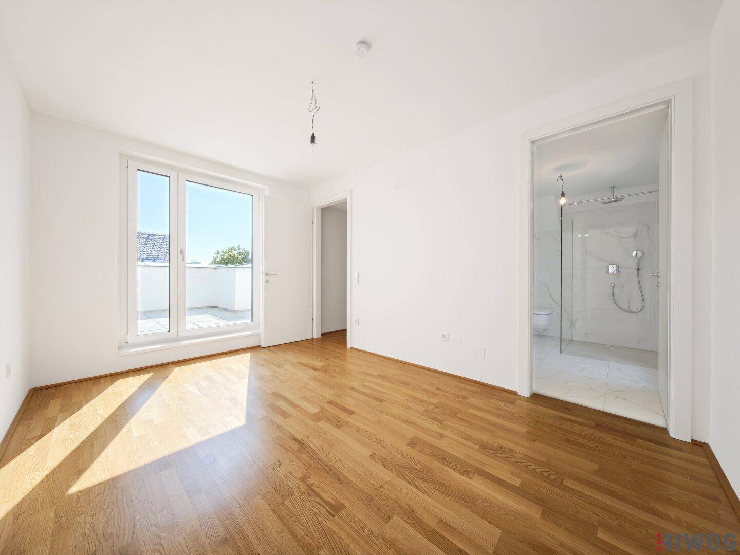 Geräumiges Schlafzimmer mit Parkettboden und direktem Zugang zu einem modernen Duschbad.