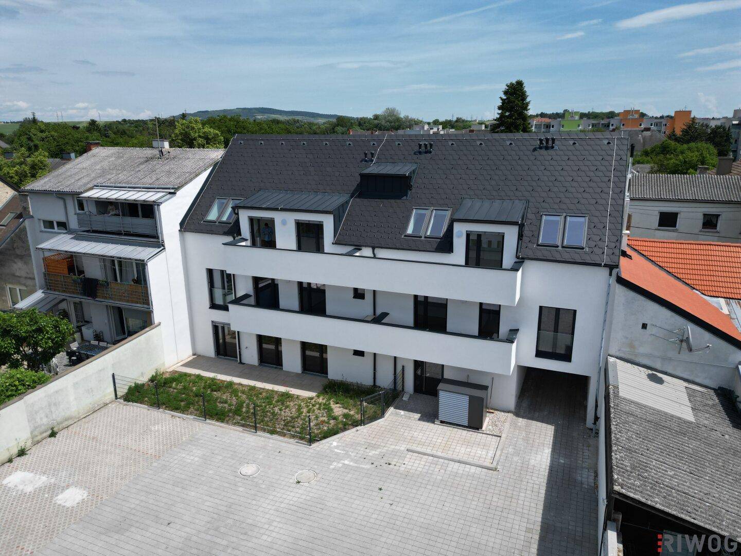 Moderne Fassade eines Neubaus mit mehreren Balkonen und dunklem Satteldach in der Wohnsiedlung.
