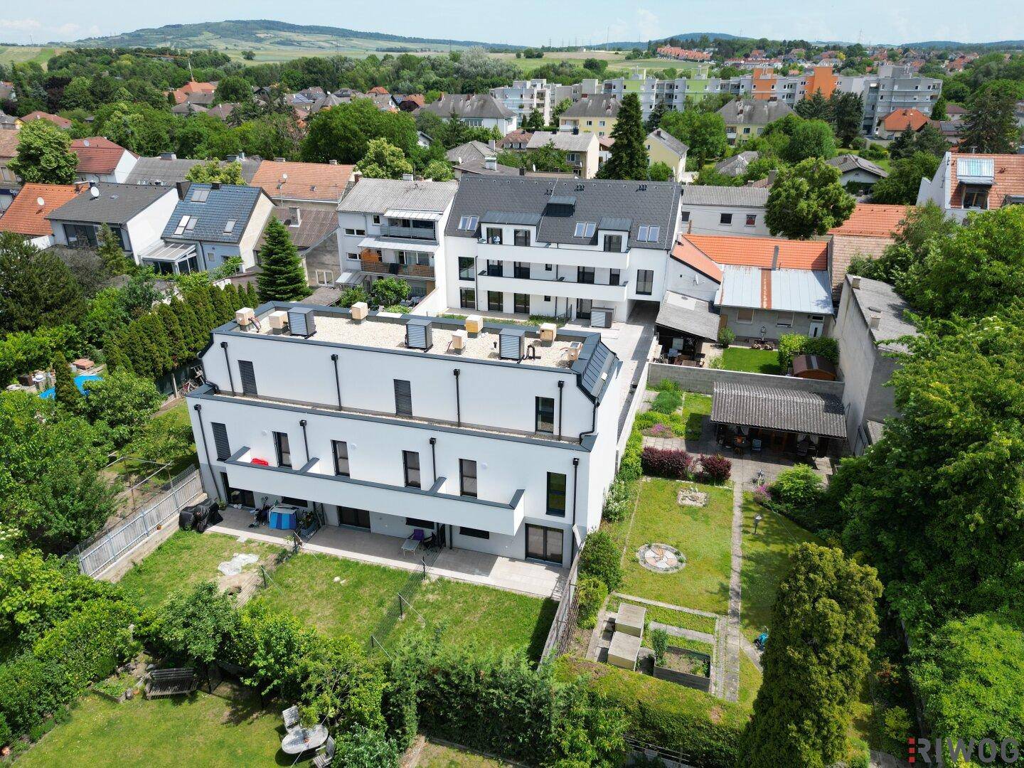 Luftaufnahme eines modernen Wohnkomplexes mit Gärten und umliegender Bebauung.