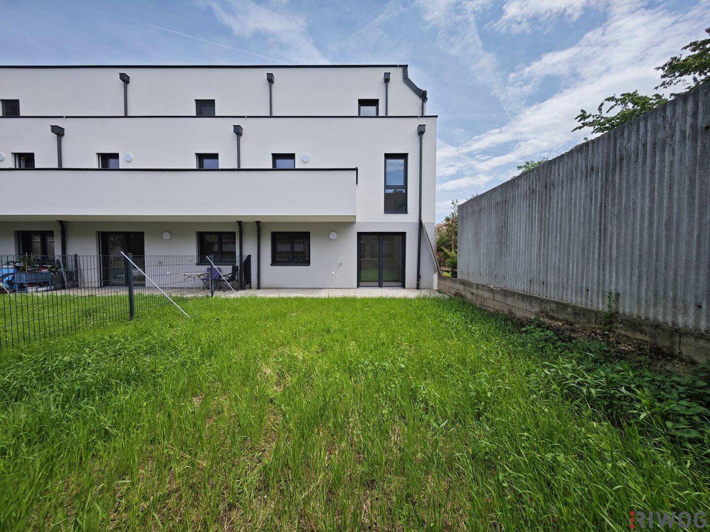 Hinterer Gartenbereich mit Rasenfläche und Blick auf die moderne Gebäudefassade.