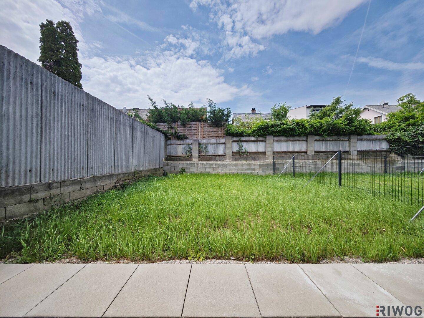 Kleiner, pflegeleichter Gartenbereich mit Rasenfläche, umgeben von einer Mauer.