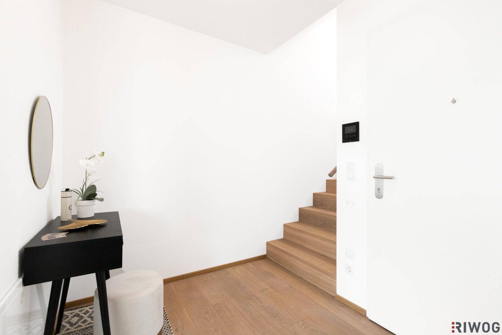 Heller Eingangsbereich mit Holzboden, Treppe und moderner Konsole.