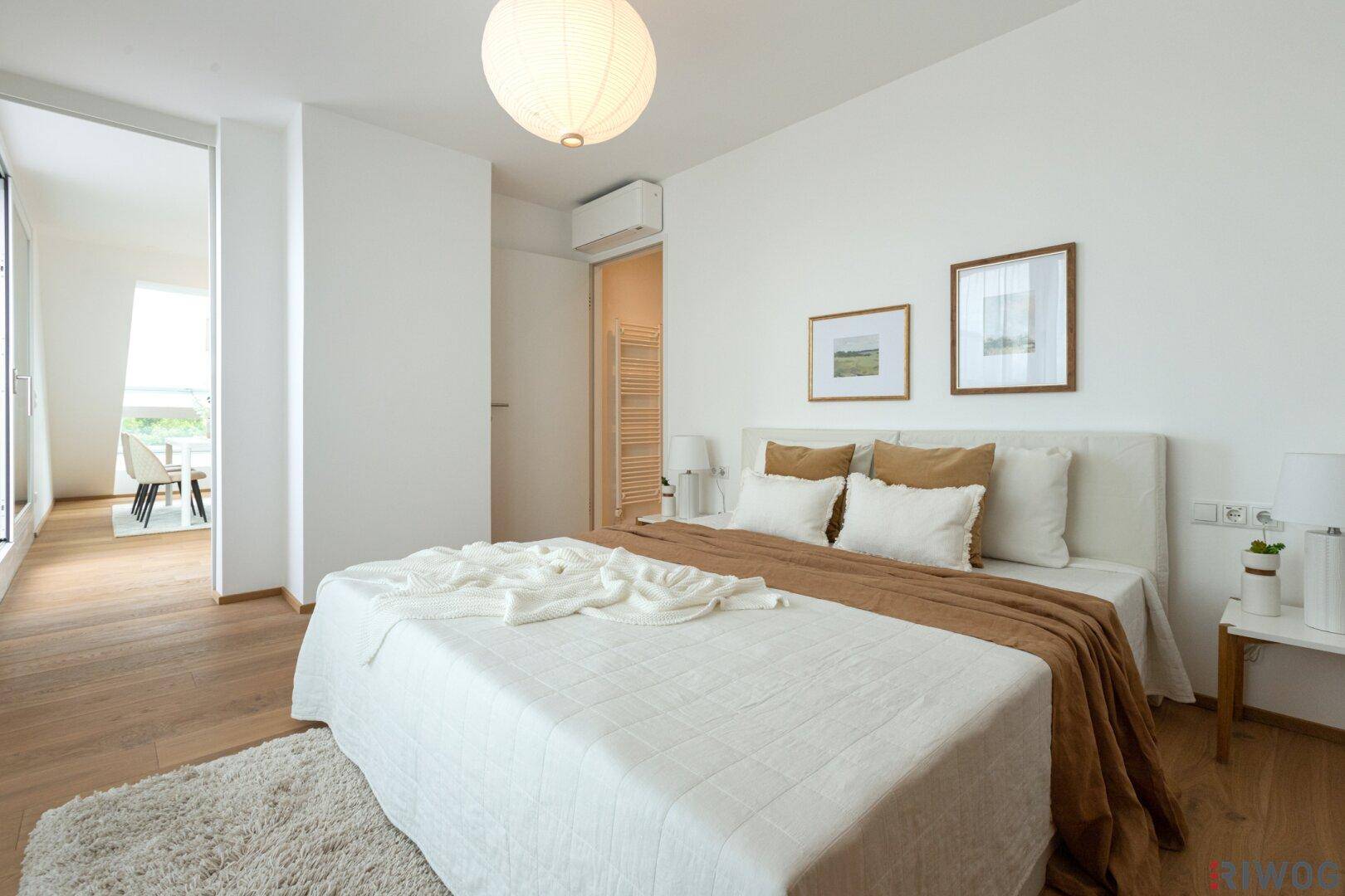 Modernes Schlafzimmer mit Holzboden, weißem Bett und Zugang zum Wohnbereich.