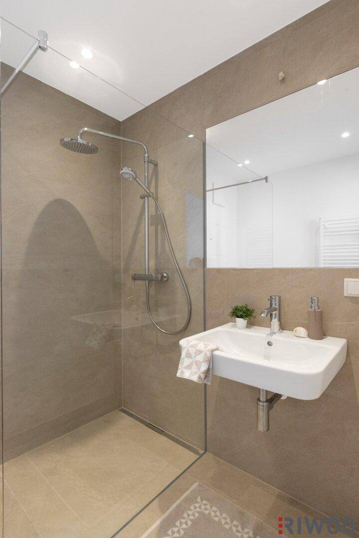 Modernes Badezimmer mit begehbarer Dusche, Wand-WC und beigen Fliesen.