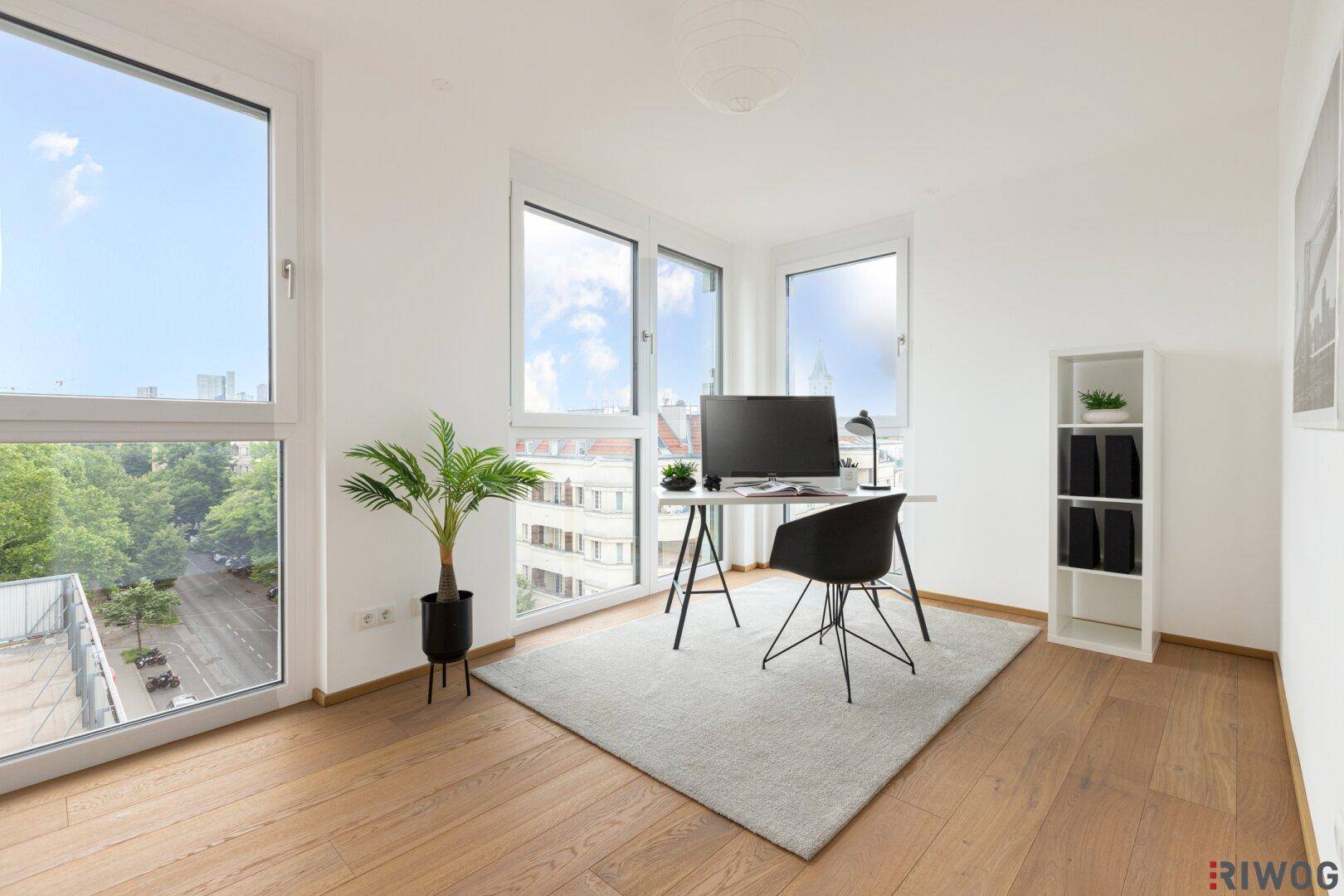 Helles Arbeitszimmer mit Holzboden, Schreibtisch und großen Fenstern mit Blick ins Grüne.