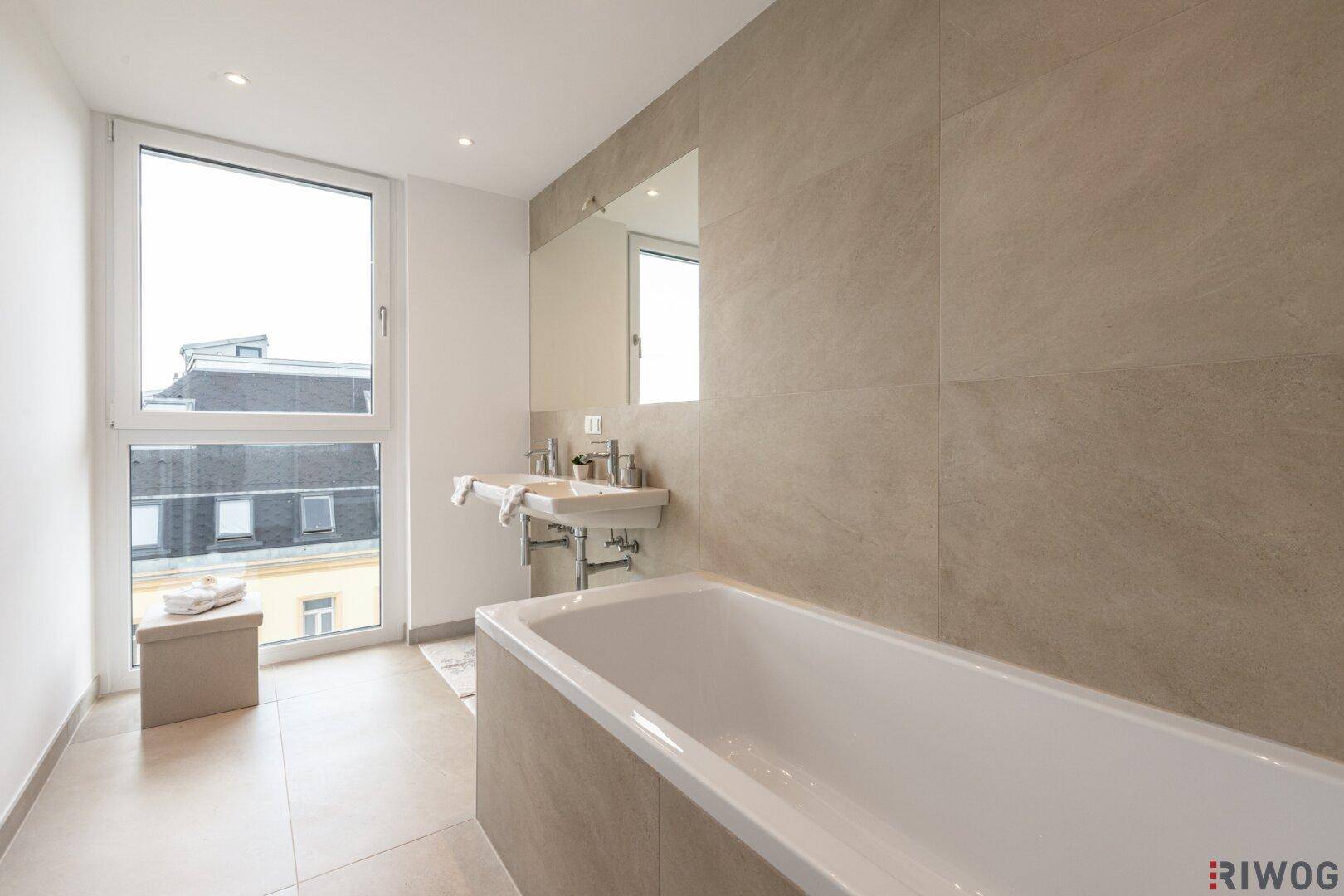 Geräumiges Badezimmer mit Badewanne, Doppelwaschbecken und großem Fenster.