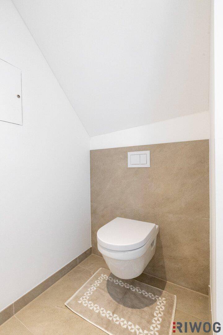 Kleines Gäste-WC mit Wand-WC und beigen Fliesen unter einer Dachschräge.