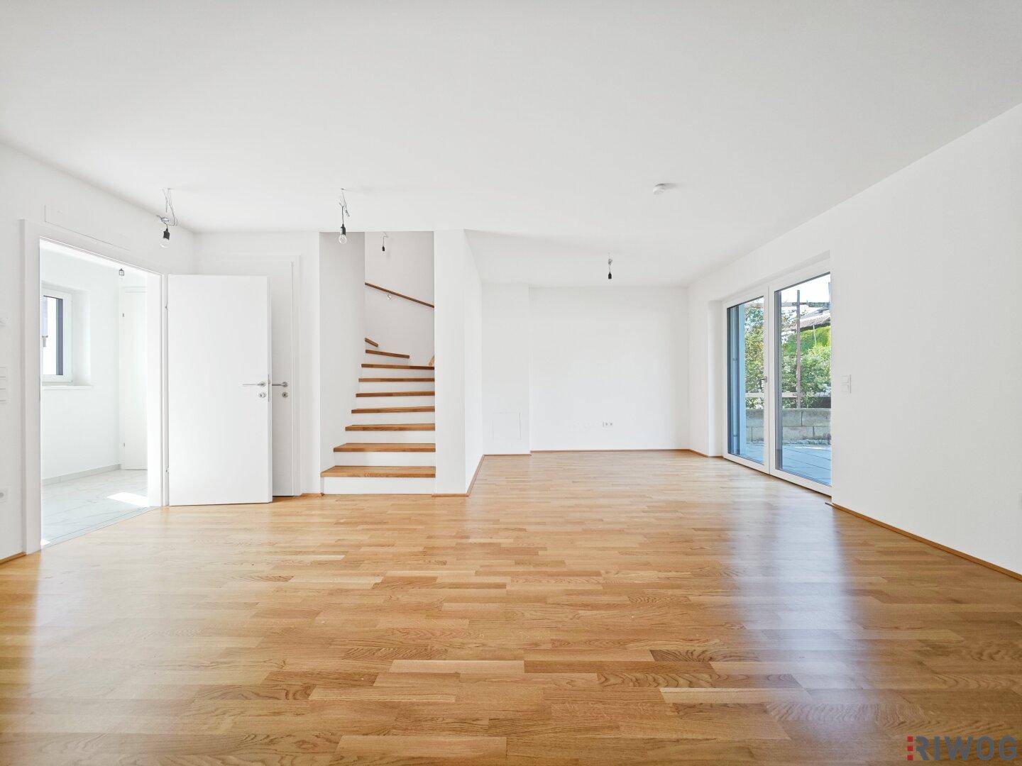 Geräumiges, helles Wohnzimmer mit Holzboden und großen Schiebetüren zum Außenbereich.