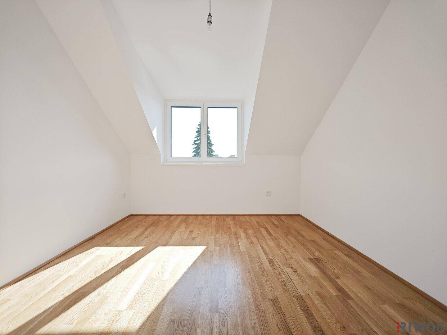 Helles Schlafzimmer im Dachgeschoss mit Holzboden und einem Fenster mit Blick ins Grüne.