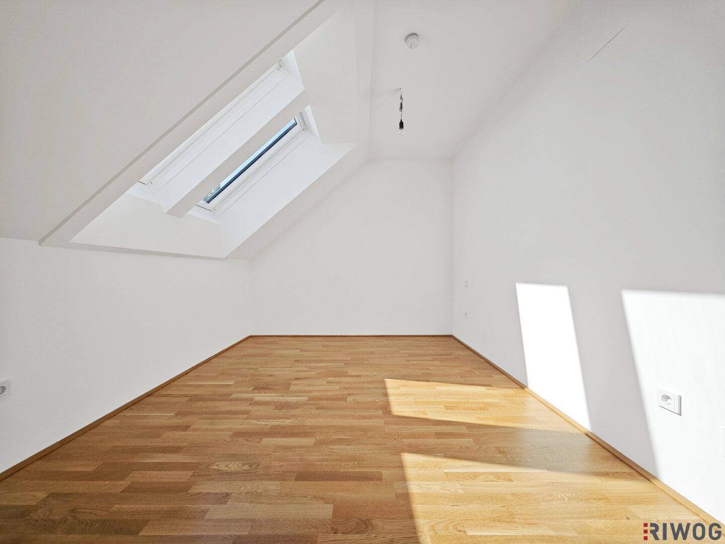 Kleinerer Dachgeschossraum mit Holzboden und einem einzelnen Dachfenster, gut beleuchtet.
