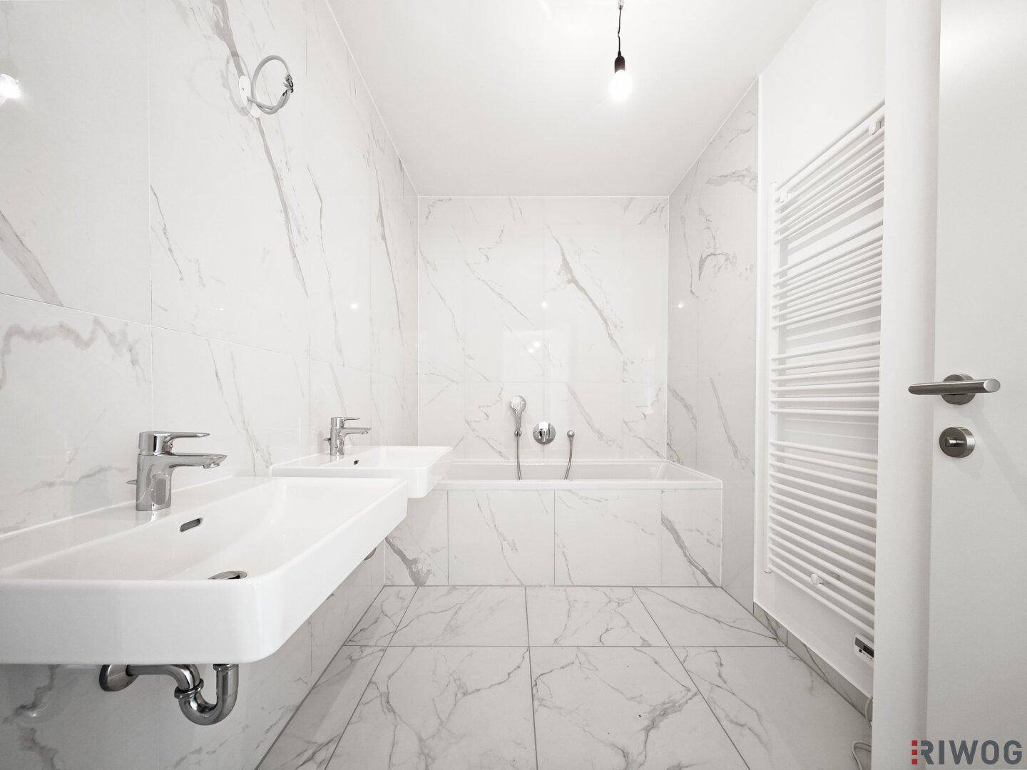 Modernes Badezimmer mit weißen Marmorfliesen, Doppelwaschbecken und integrierter Badewanne.