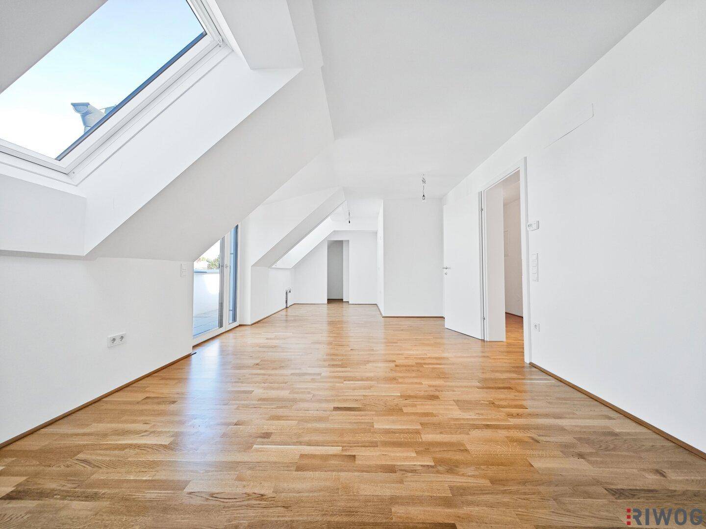 Geräumiges Dachgeschosszimmer mit hellem Holzboden, schrägen Wänden und einem großen Dachfenster.