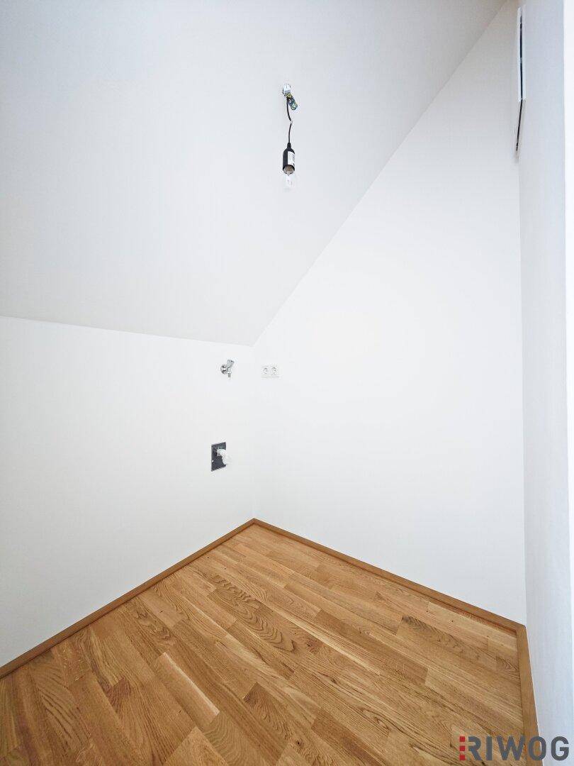 Ecke eines Raumes im Dachgeschoss mit Holzboden und schrägen Wänden, gut beleuchtet.