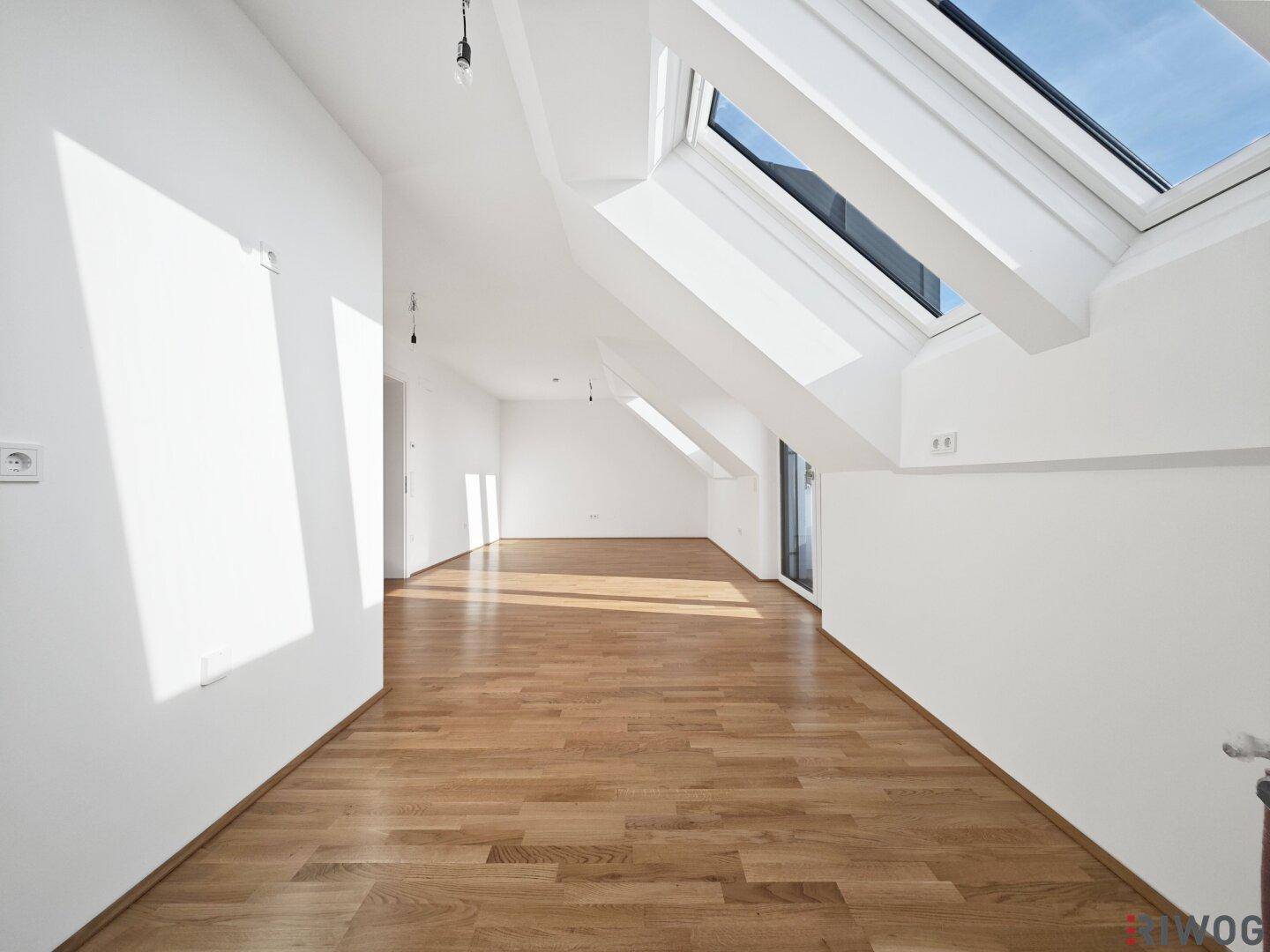Helles und geräumiges Dachgeschosszimmer mit Holzboden und großen Dachfenstern, ideal für Wohnzwecke.