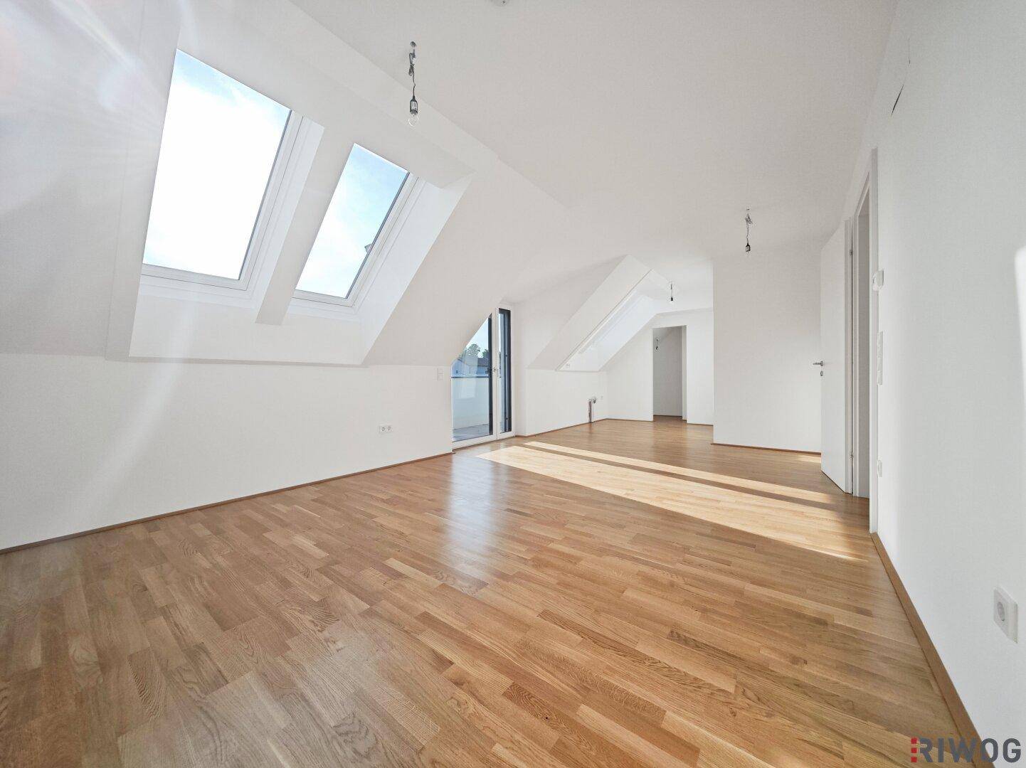 Lichtdurchfluteter Dachgeschossraum mit Holzboden, mehreren Dachfenstern und Zugang zu einem Balkon.