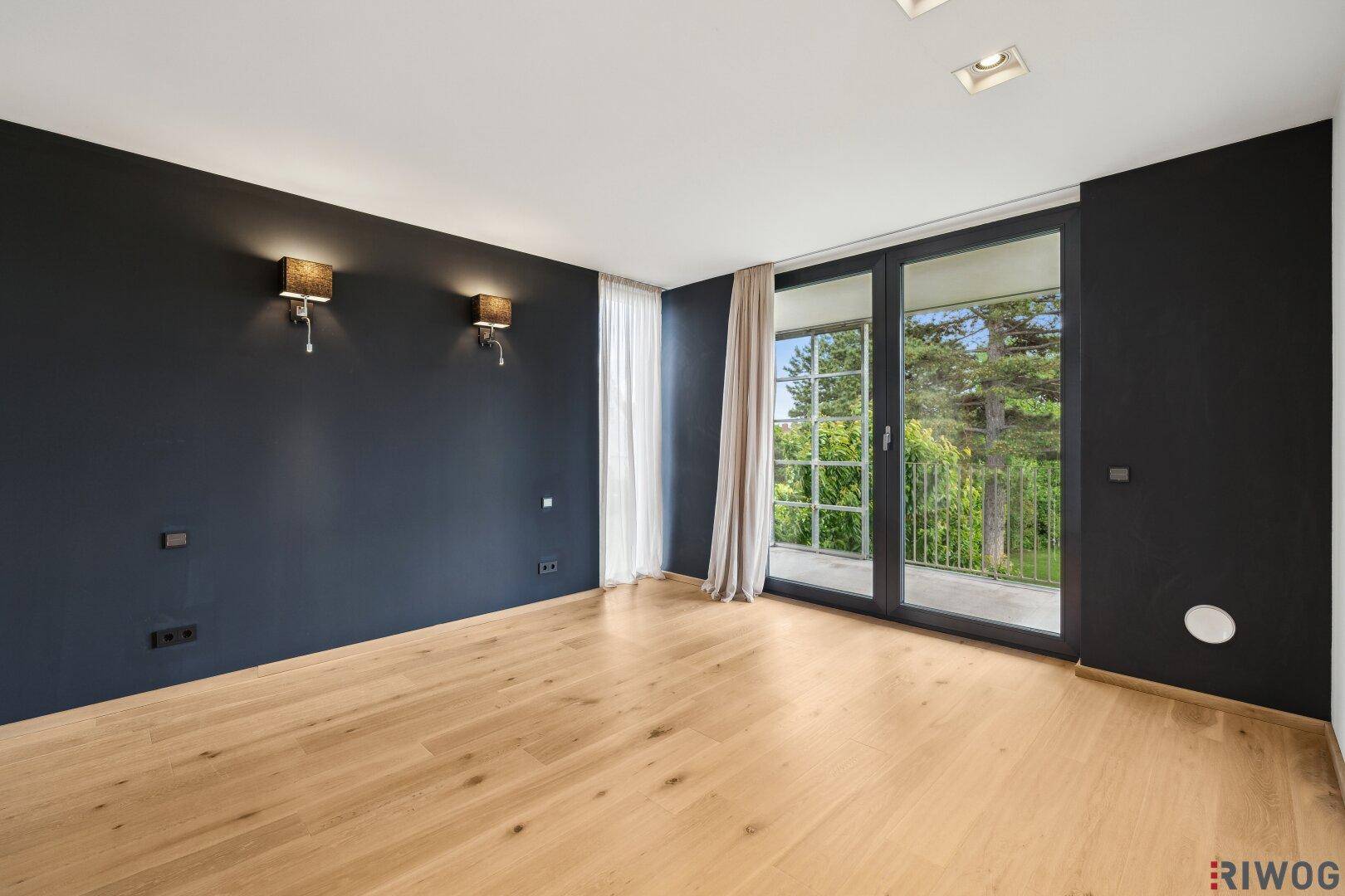 Geräumiger Wohnbereich mit dunklen Wänden, hellem Holzboden und Zugang zu einem Balkon.