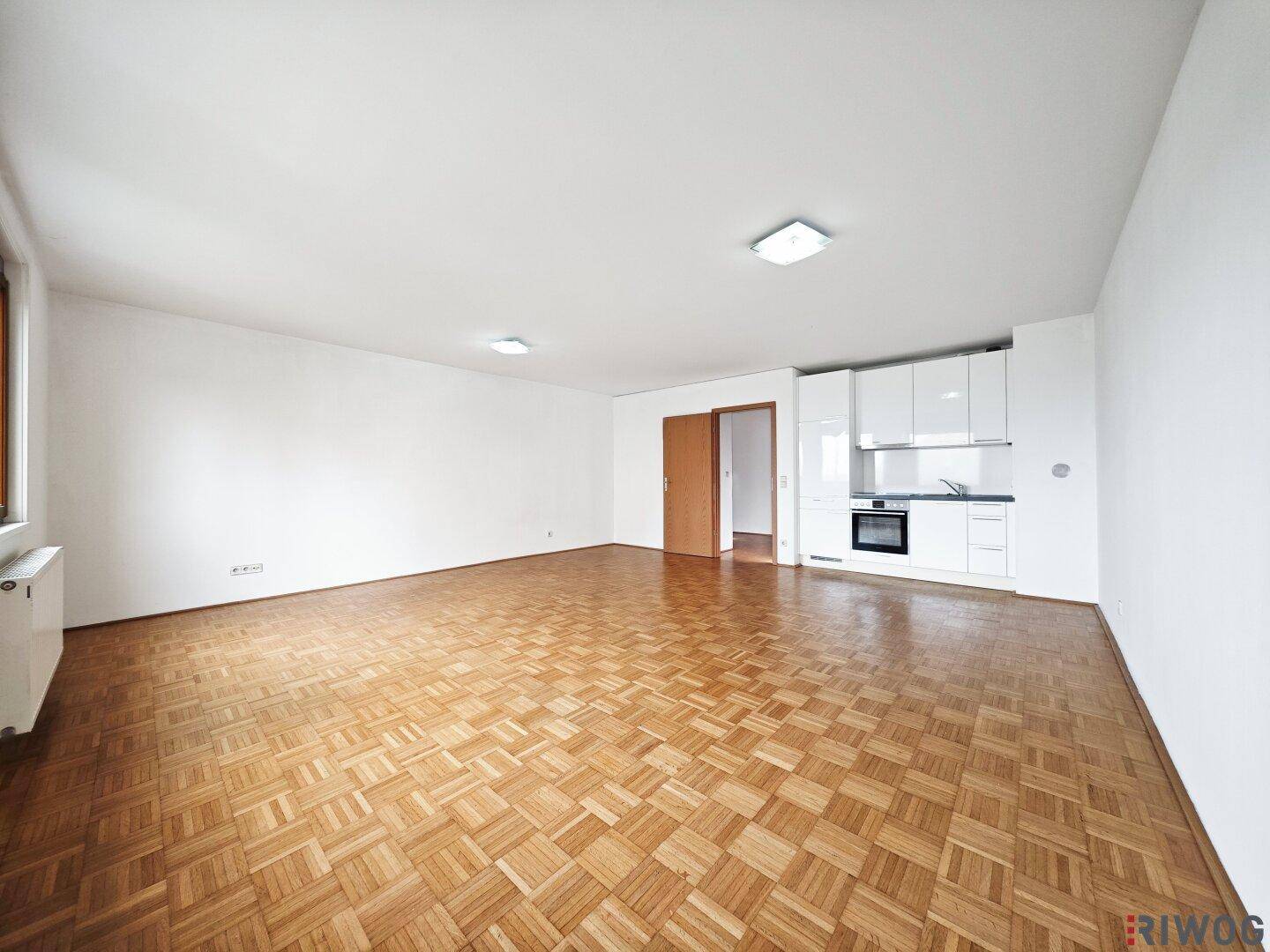 Helles Wohnzimmer mit integrierter Küchenzeile und Parkettboden, ideal für offenes Wohnen.