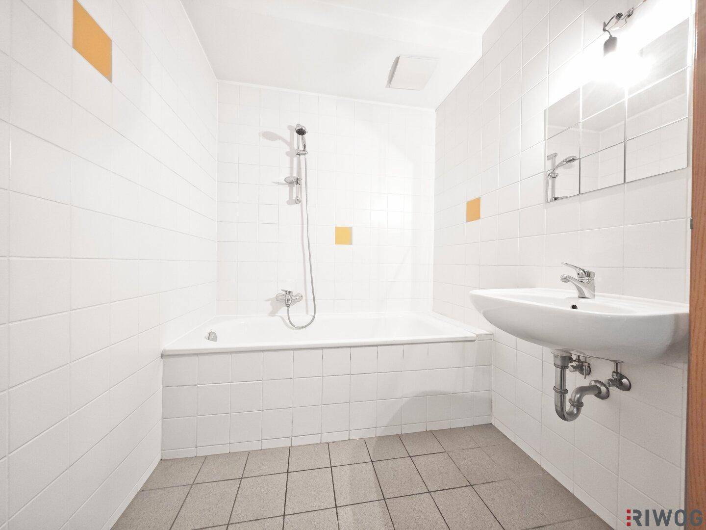Funktionales Badezimmer mit Badewanne, Dusche und weiß gefliesten Wänden, mit gelben Akzenten.