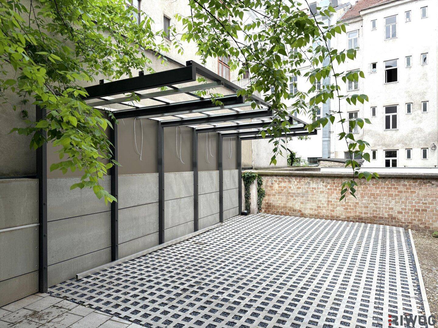 Überdachter Parkplatz mit Gittersteinen und umgebenden Mauern.