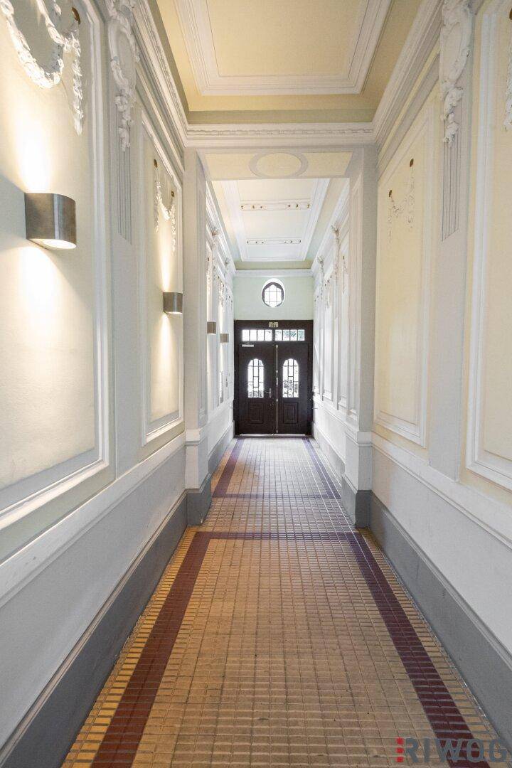 Historischer Hausflur mit aufwendigen Stuckarbeiten, Wandbeleuchtung und gemustertem Boden.