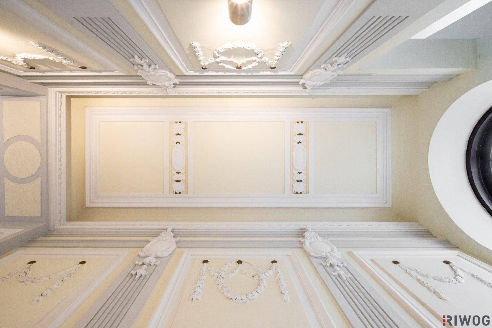Detailaufnahme einer kunstvollen Stuckdecke mit klassischen Verzierungen und Beleuchtung.