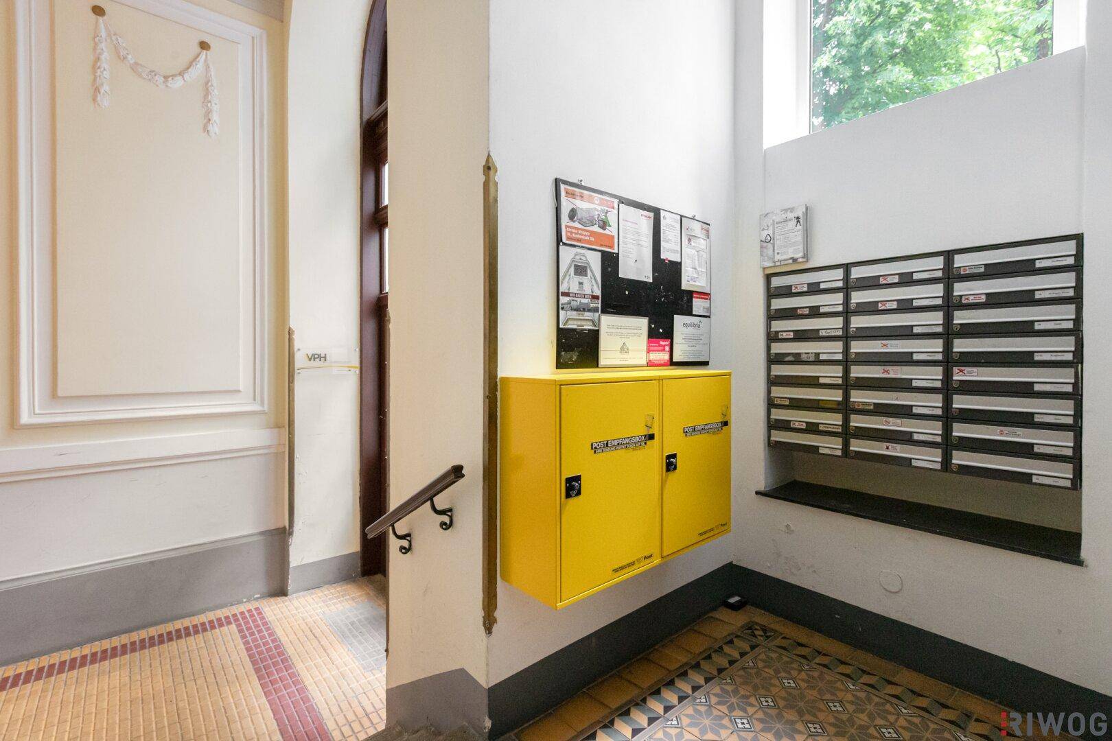 Eingangsbereich mit Briefkästen, gelben Schränken und dekorativem Stuck an der Wand.