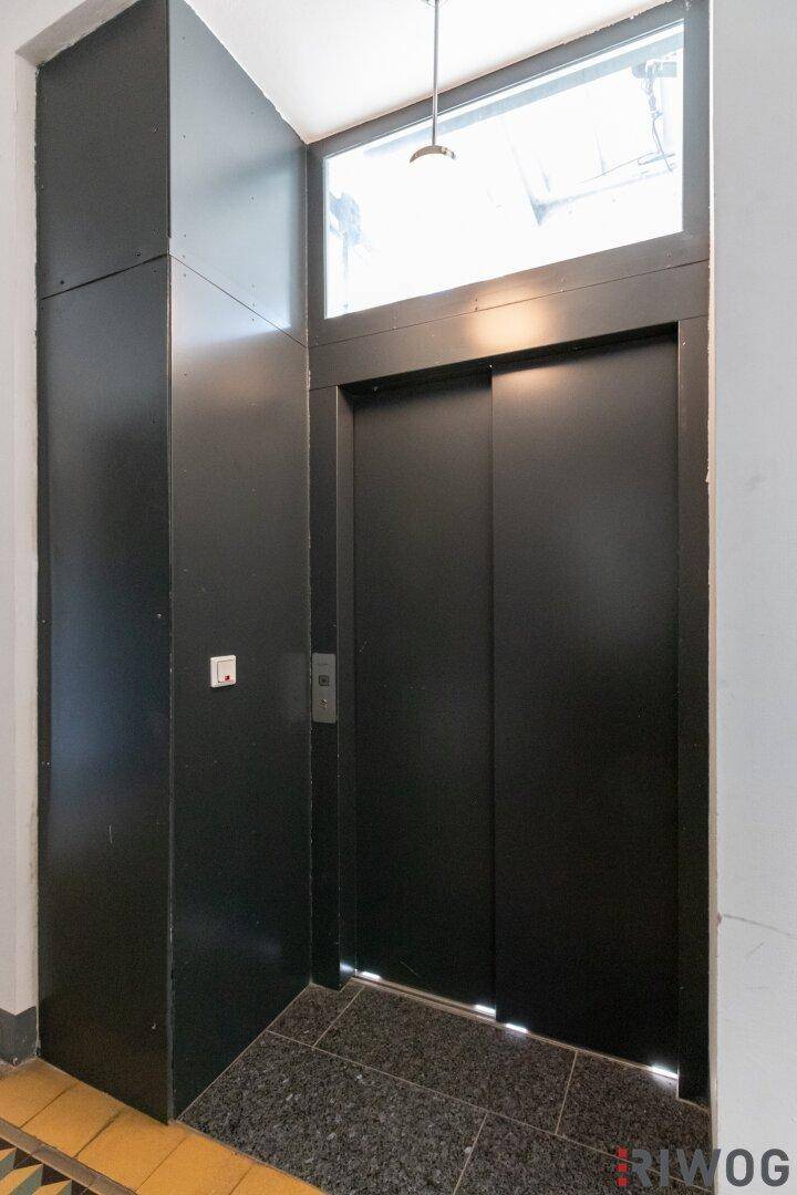 Moderner Aufzug mit schwarzen Türen und Fenster über dem Eingangsbereich.