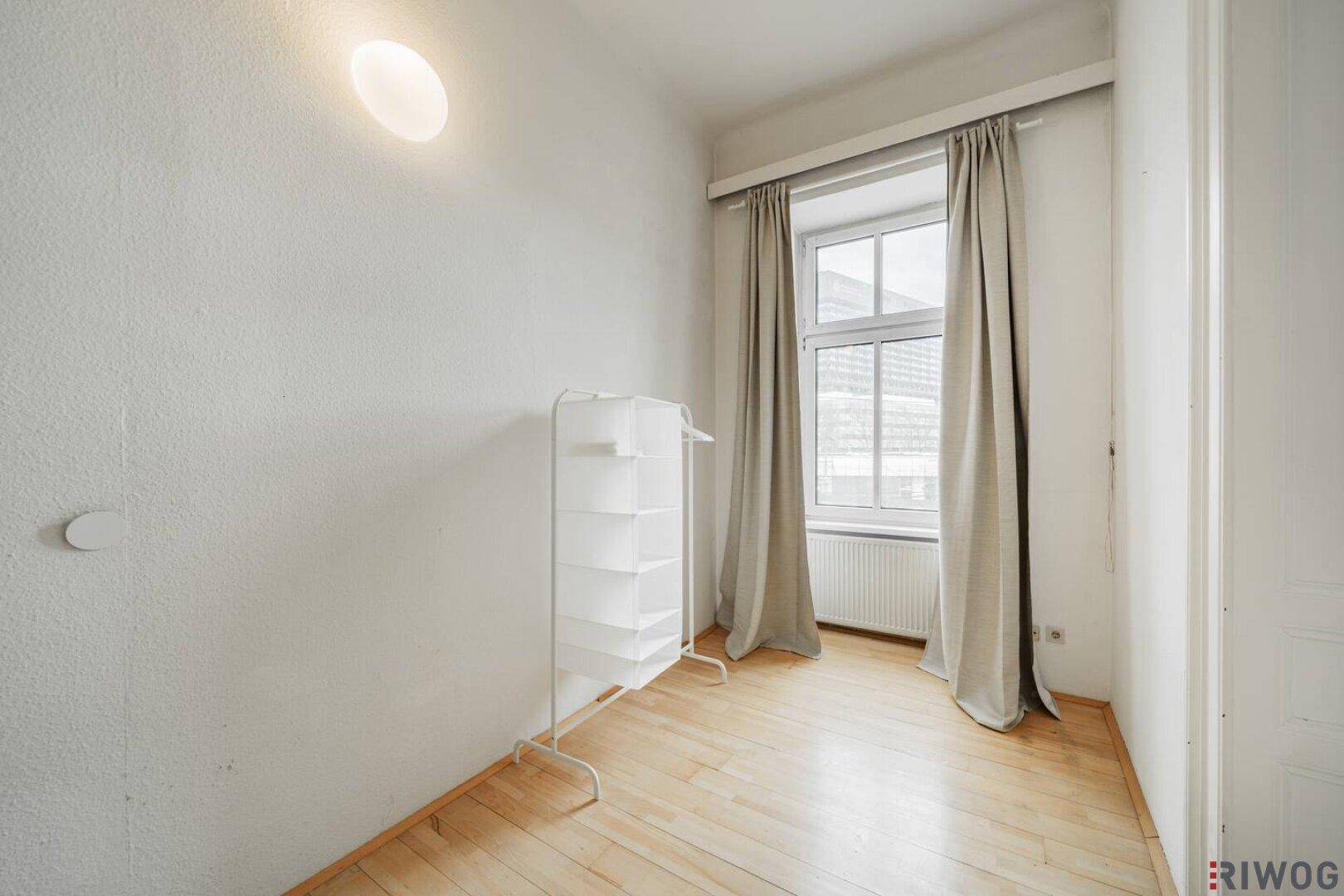 Helles Schlafzimmer mit großem Fenster, Vorhängen und einem praktischen Kleiderständer.