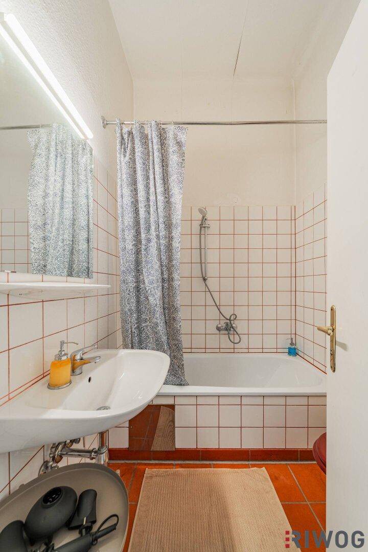 Badezimmer mit Badewanne, Duschvorhang, Waschbecken und Fliesen in Weiß und Terrakotta.