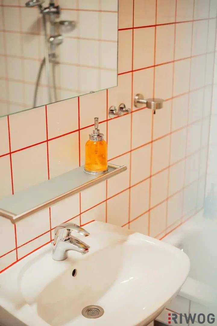 Detailansicht des Waschbeckens im Badezimmer mit weißen Fliesen und roten Fugen.