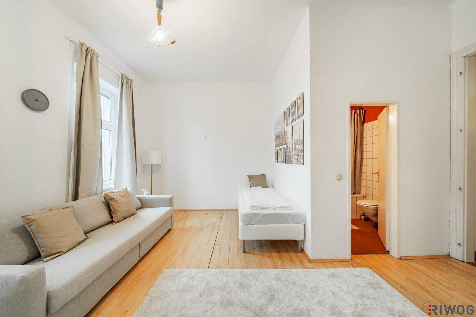 Geräumiges Wohnzimmer mit Holzboden und Zugang zu einem kleinen Badezimmer.