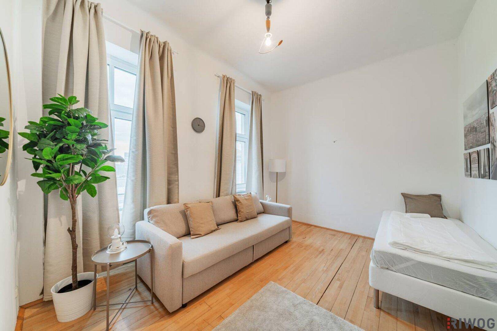 Helles Wohnzimmer mit Schlafsofa, Einzelbett und Holzboden, ideal für Gäste oder als Studio.