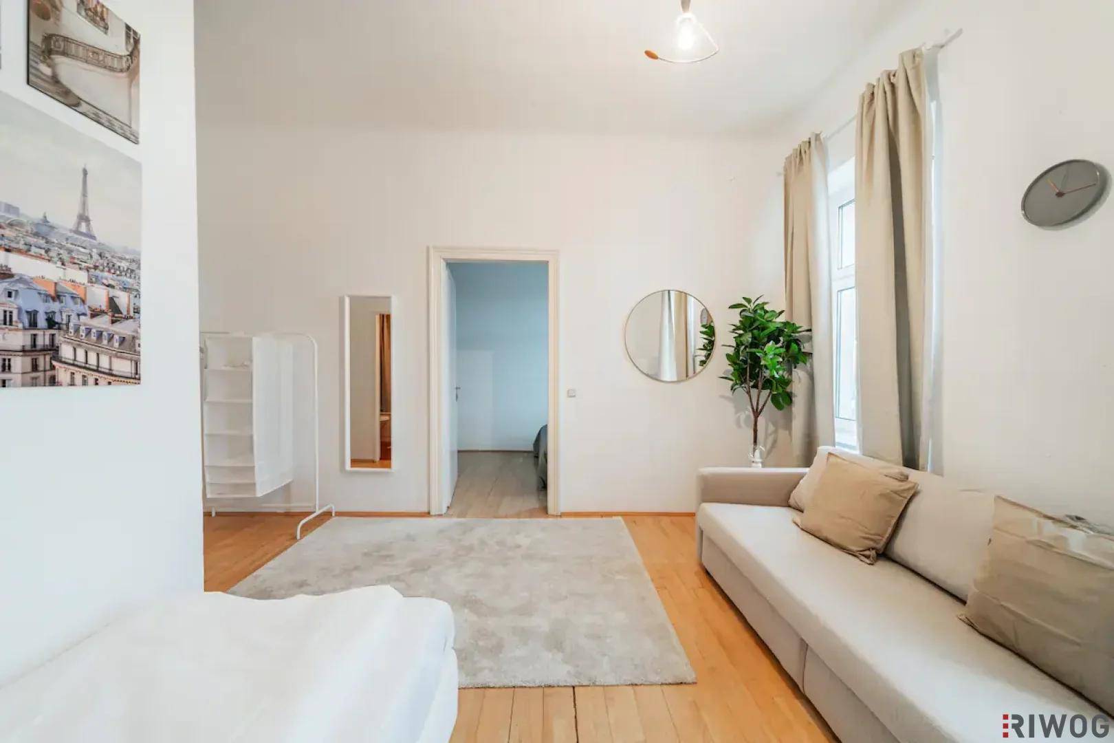 Helles Wohnzimmer mit Holzboden, beigem Sofa und Zugang zu einem weiteren Raum.