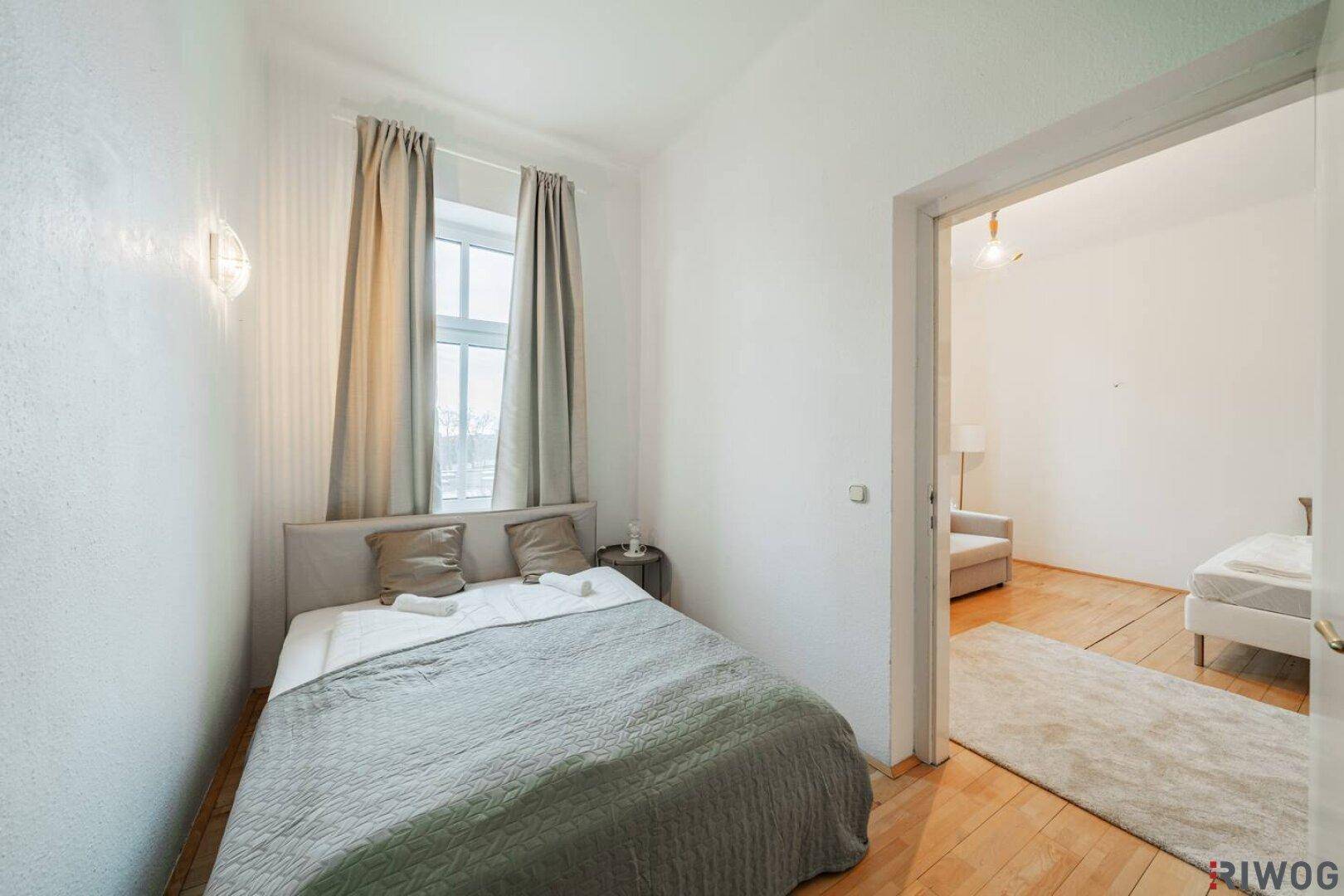 Gemütliches Schlafzimmer mit Doppelbett, Holzboden und Zugang zum angrenzenden Wohnzimmer.
