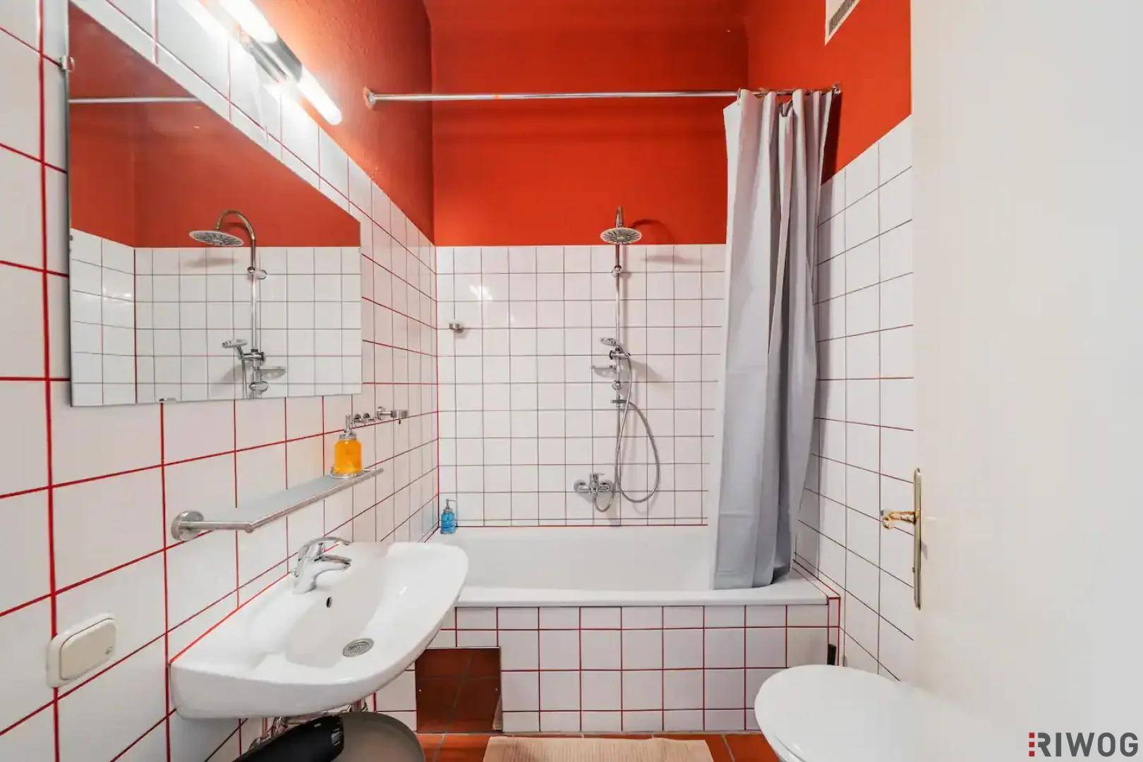 Badezimmer mit weißen Fliesen, roten Fugen und Wänden sowie einer Badewanne mit Duschfunktion.