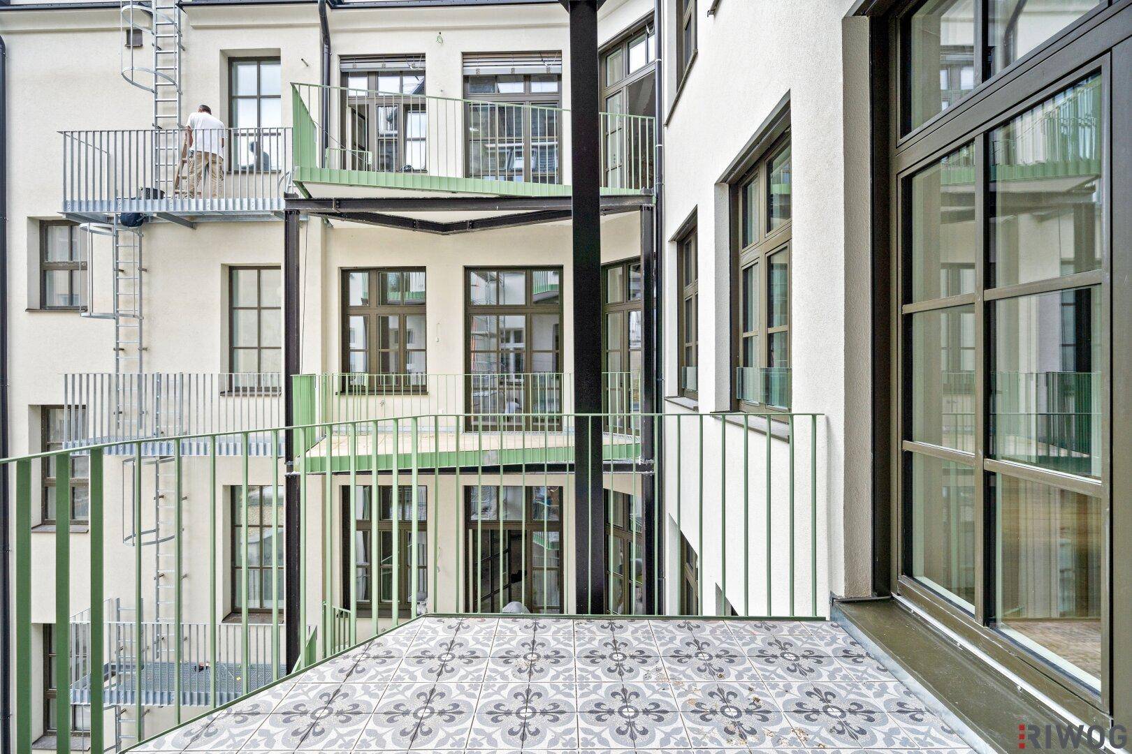 Balkon mit dekorativen Fliesen und Blick in den ruhigen Innenhof, umgeben von weiteren Balkonen und großen Fenstern.