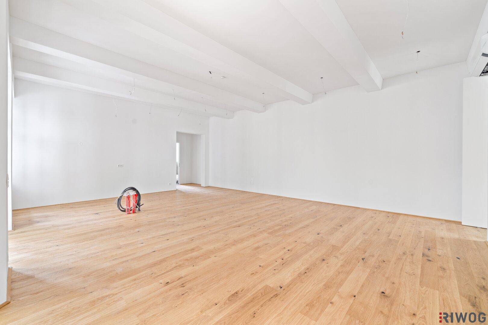 Geräumiger, heller Wohnbereich mit Holzboden und sichtbaren Deckenbalken.